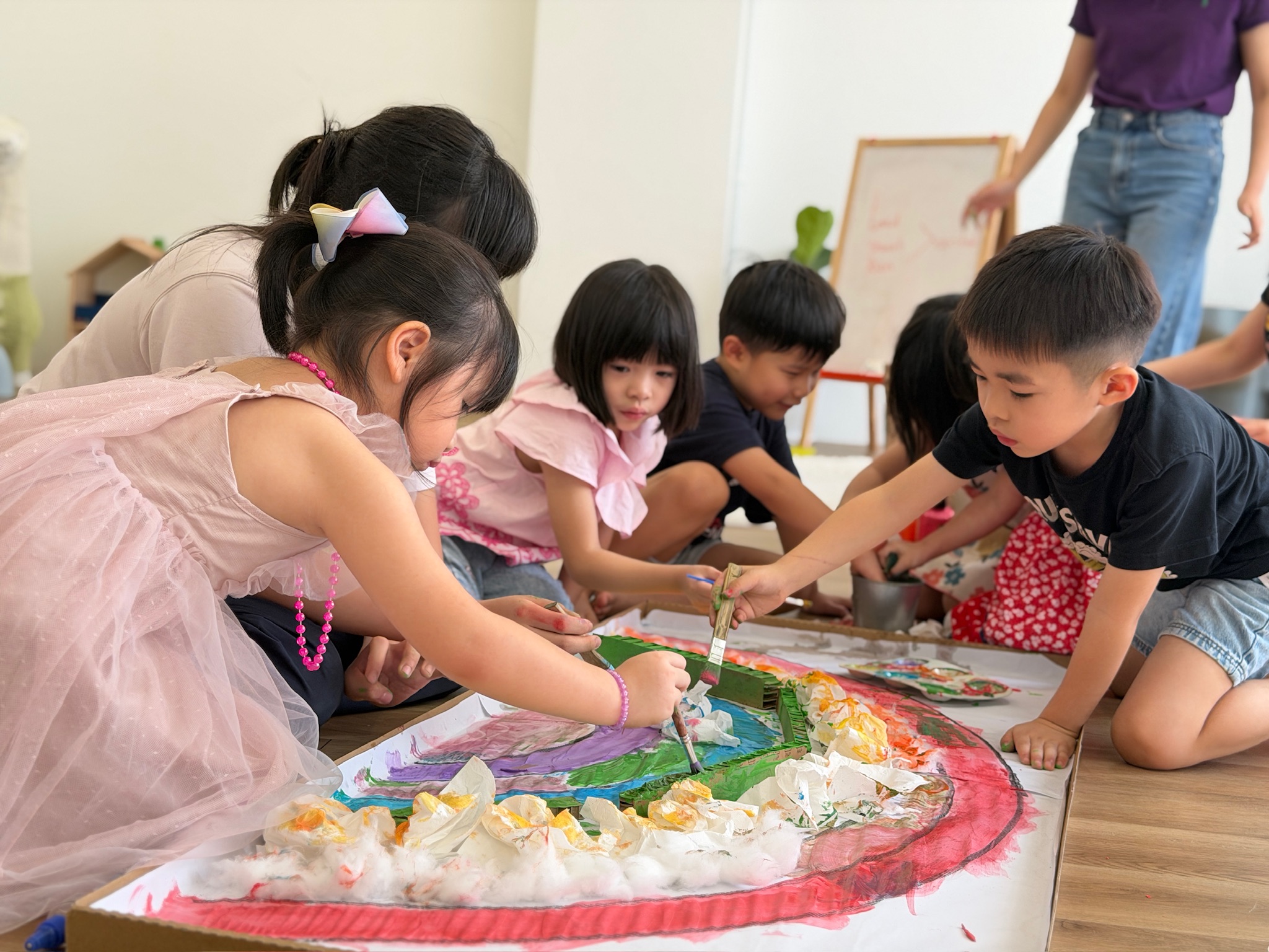 Children painting a large rainbow mural together on the floor